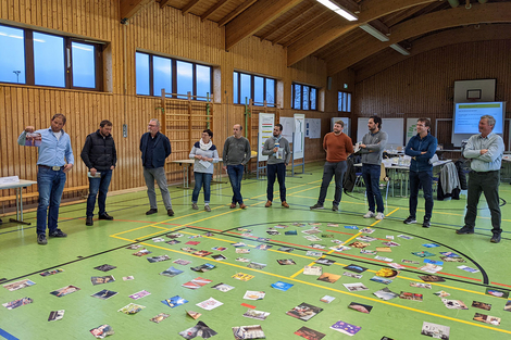 Leute in Turnhalle um Bilder am Boden herum