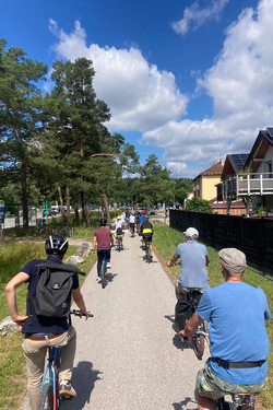 Mehrere Personen fahren mit Fahrrädern einen Weg zwischen Bäumen und Häusern entlang