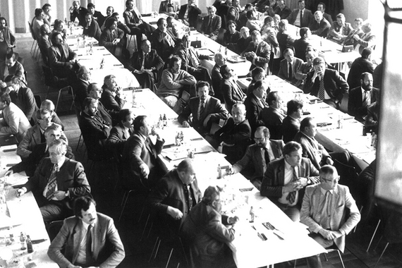 Schwarz-Weiß Foto mit Tischreihen und vielen Männern in Anzügen