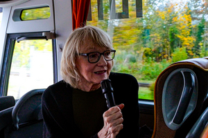 Ruth-Maria Schittich sitzt im Bus und spricht in ein Handmikrofon.