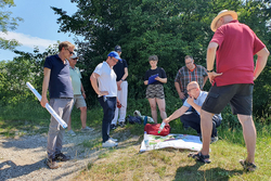 Menschen stehen um einen am Boden liegenden Plan herum und sprechen miteinander