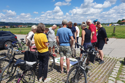 Gruppe von Menschen im Gespräch zu einem Plan, der vor ihnen auf dem Boden liegt. Daneben stehen Fahrräder