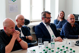 Teilnehmerinnen und Teilnehmer sitzen am Tisch und hören zu