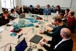 Teilnehmerinnen und Teilnehmer sitzen am Tisch und diskutieren