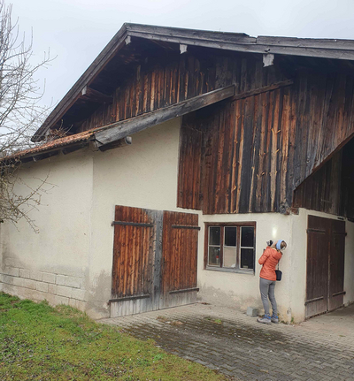 Person vor altem Bauernhof leuchtet mit Taschenlampe hoch zum Dach