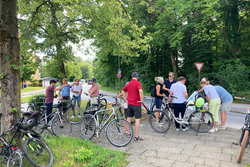 Eine Gruppe von Menschen stehen mit ihren Fahrrädern auf dem Gehweg und sind im Gespräch 